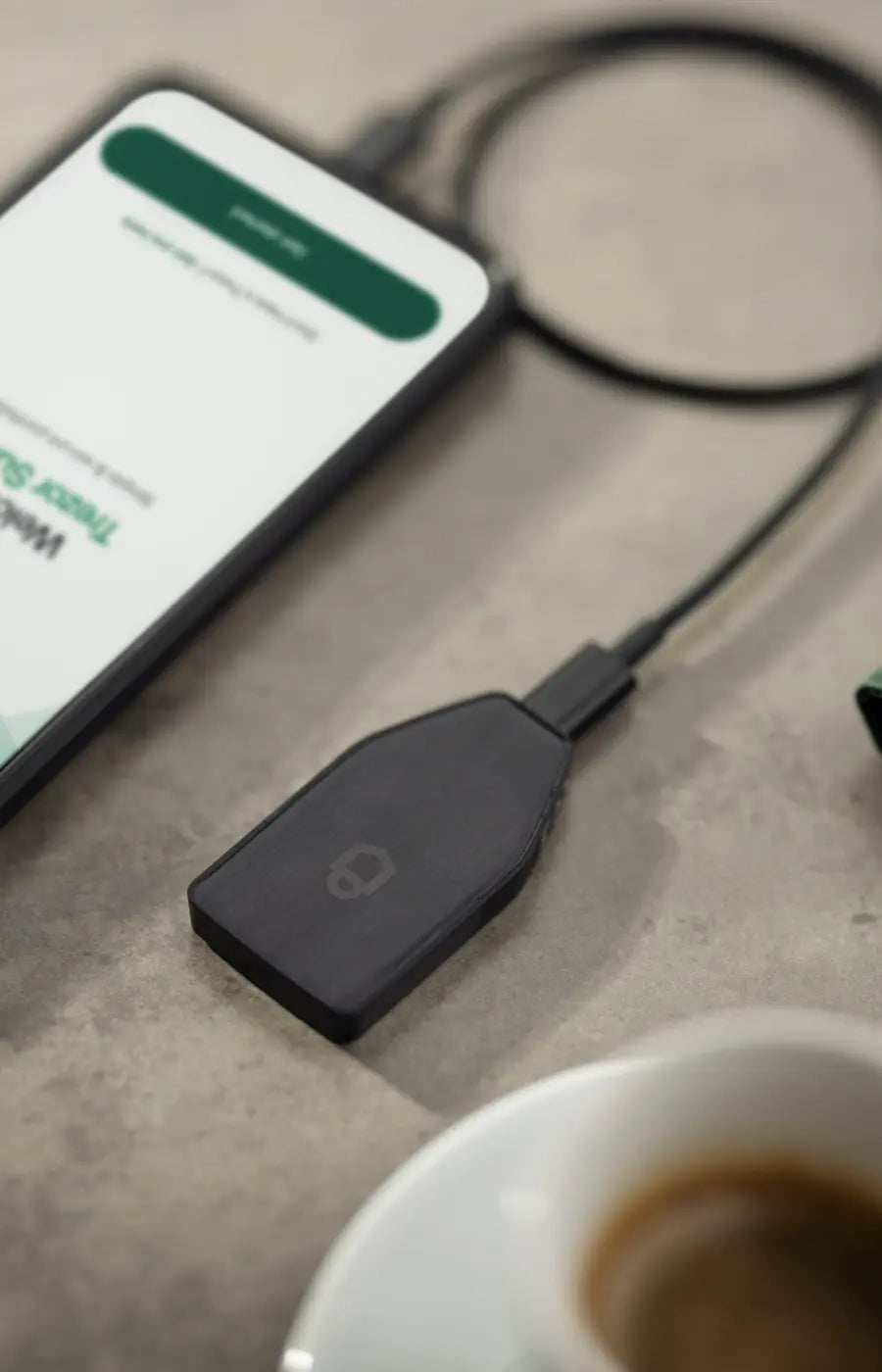 Trezor Safe 3 cold wallet facedown on a surface next to a laptop and a coffee.