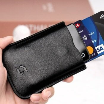 Hand holding a SafePal leather wallet with a SafePal S1 cold wallet and multiple credit cards visibly poking out.